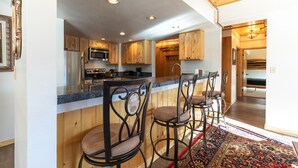 Una cocina con armarios de madera, un refrigerador de acero inoxidable, un microondas y una barra con taburetes.