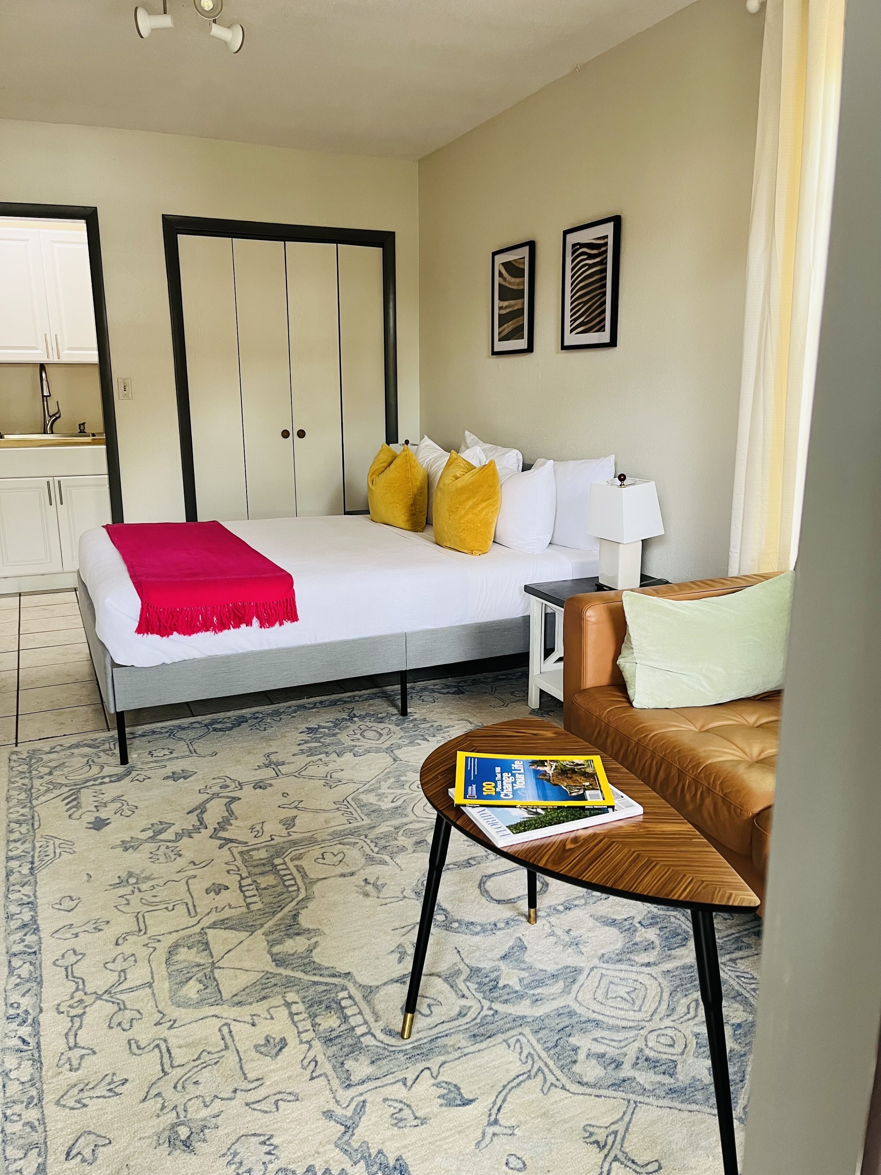 A hotel room with a bed, a sofa, a small table, a nightstand, a lamp, and a window with curtains.