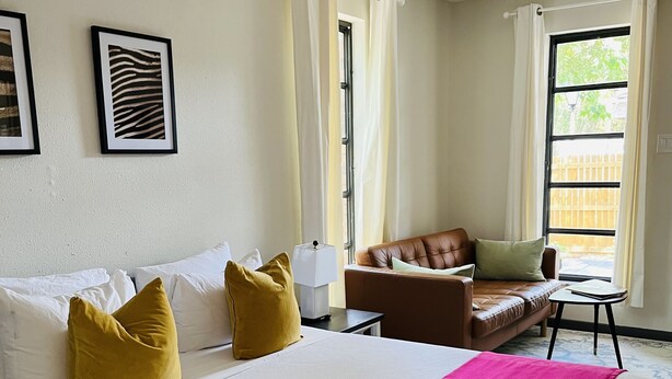 A hotel room with a large bed, a brown leather sofa, a small table, and a window with curtains. - Beautiful suite with separate entrance. (New Port Richey)