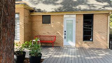 A brick building with a wooden deck, a red bench, and two potted plants.