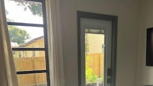 A living room with a brown leather sofa, a small table, and a sliding glass door leading to a backyard with a wooden fence and potted plants. - Beautiful suite with separate entrance. (New Port Richey)