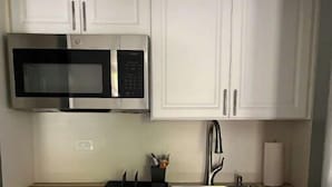 A compact kitchen with white cabinets, a stainless steel microwave, a built-in refrigerator, and a wooden countertop. - Beautiful suite with separate entrance. (New Port Richey)