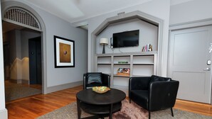 A modern living room with a round table, two black leather sofas, a mounted TV, and a bookshelf.