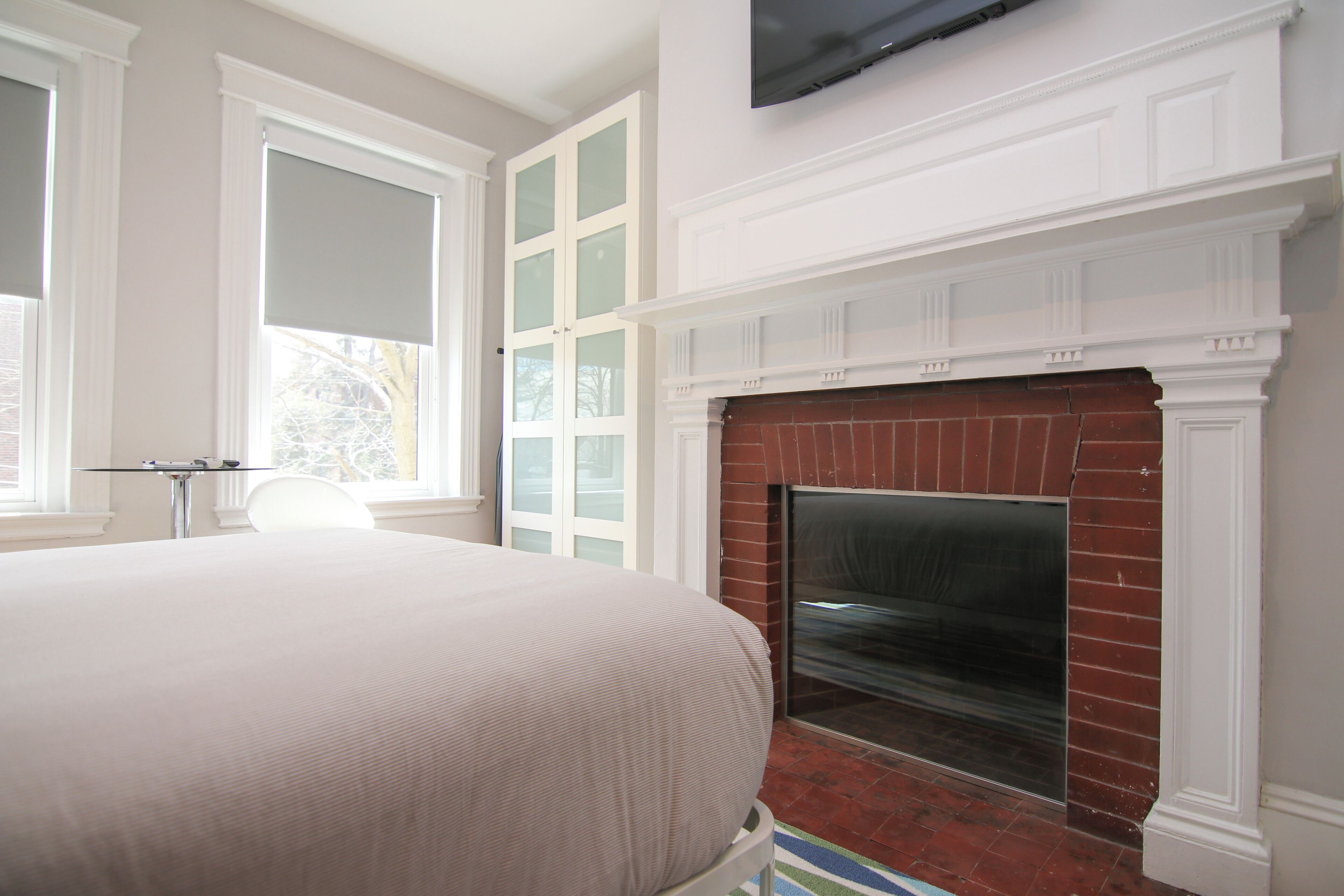 A bedroom with a large bed, a fireplace, and a TV mounted on the wall.