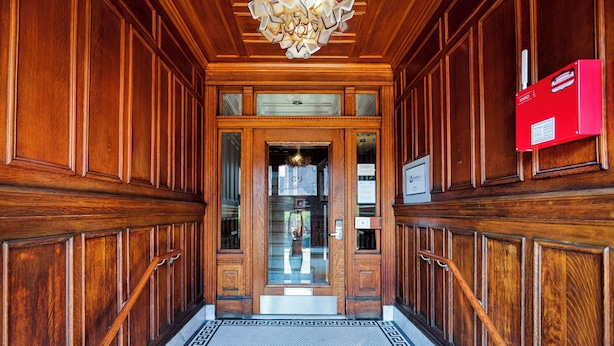 A wooden hallway with a patterned floor leading to a door.
