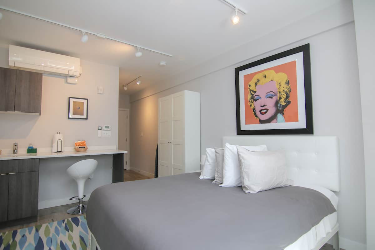 A modern hotel room with a large bed, a white headboard, and a framed pop art print on the wall.