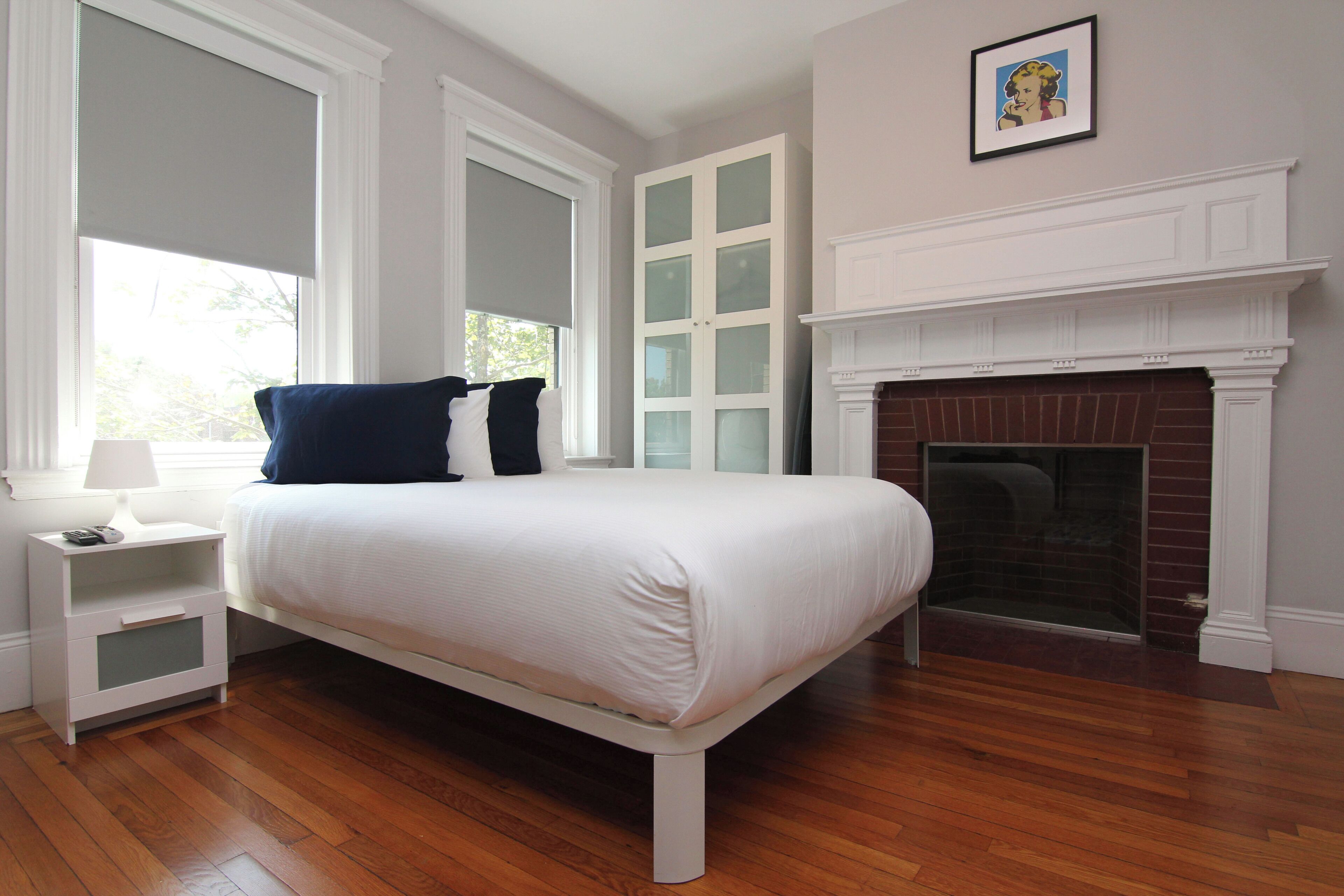 Un dormitorio con cama, mesita de noche, chimenea y ventanas amplias.