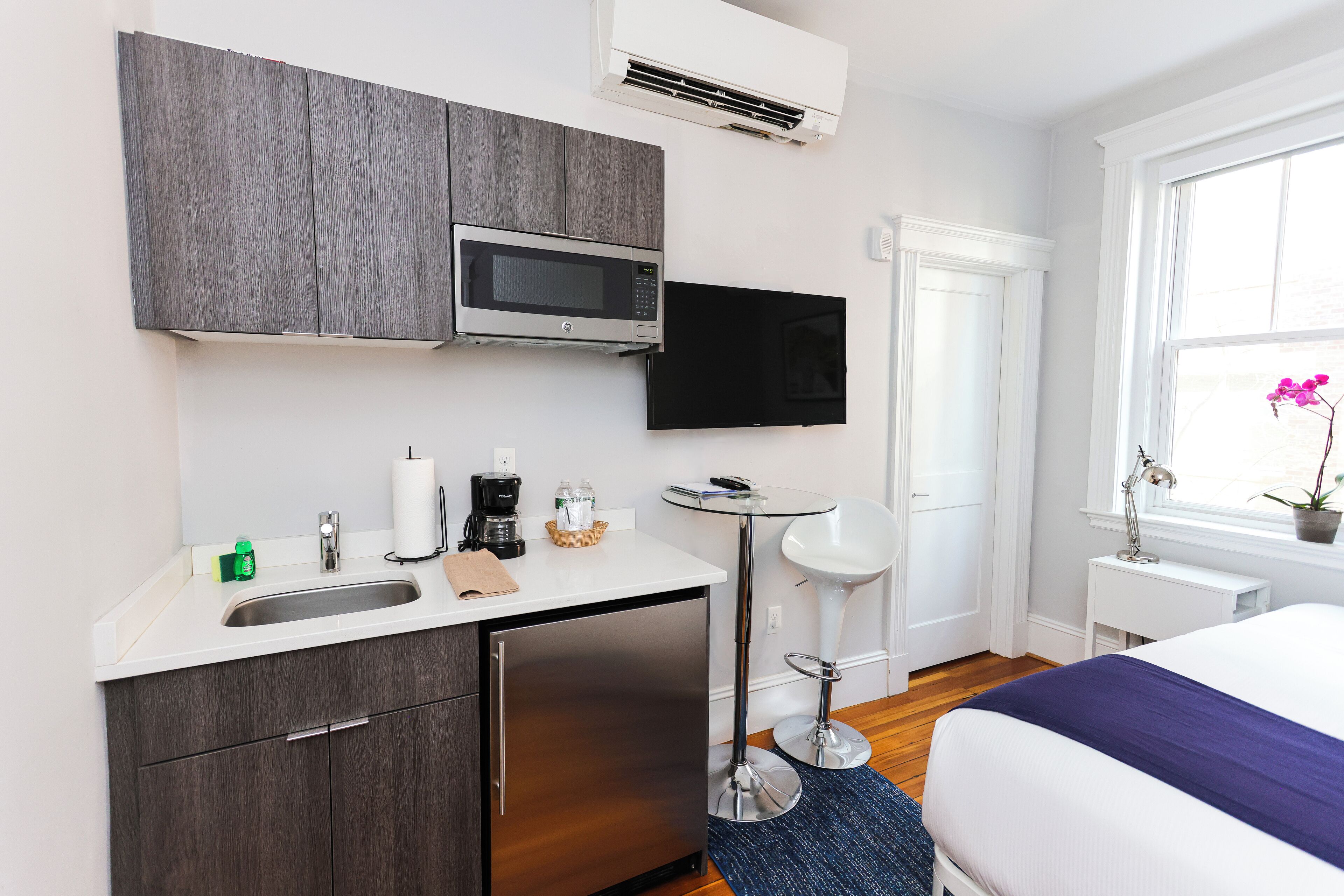 Ett kompakt hotellrum med ett litet pentry, en säng, ett litet matbord och ett fönster med utsikt.