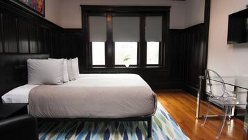 A bedroom with a bed, a chair, a TV, and a window with blinds.