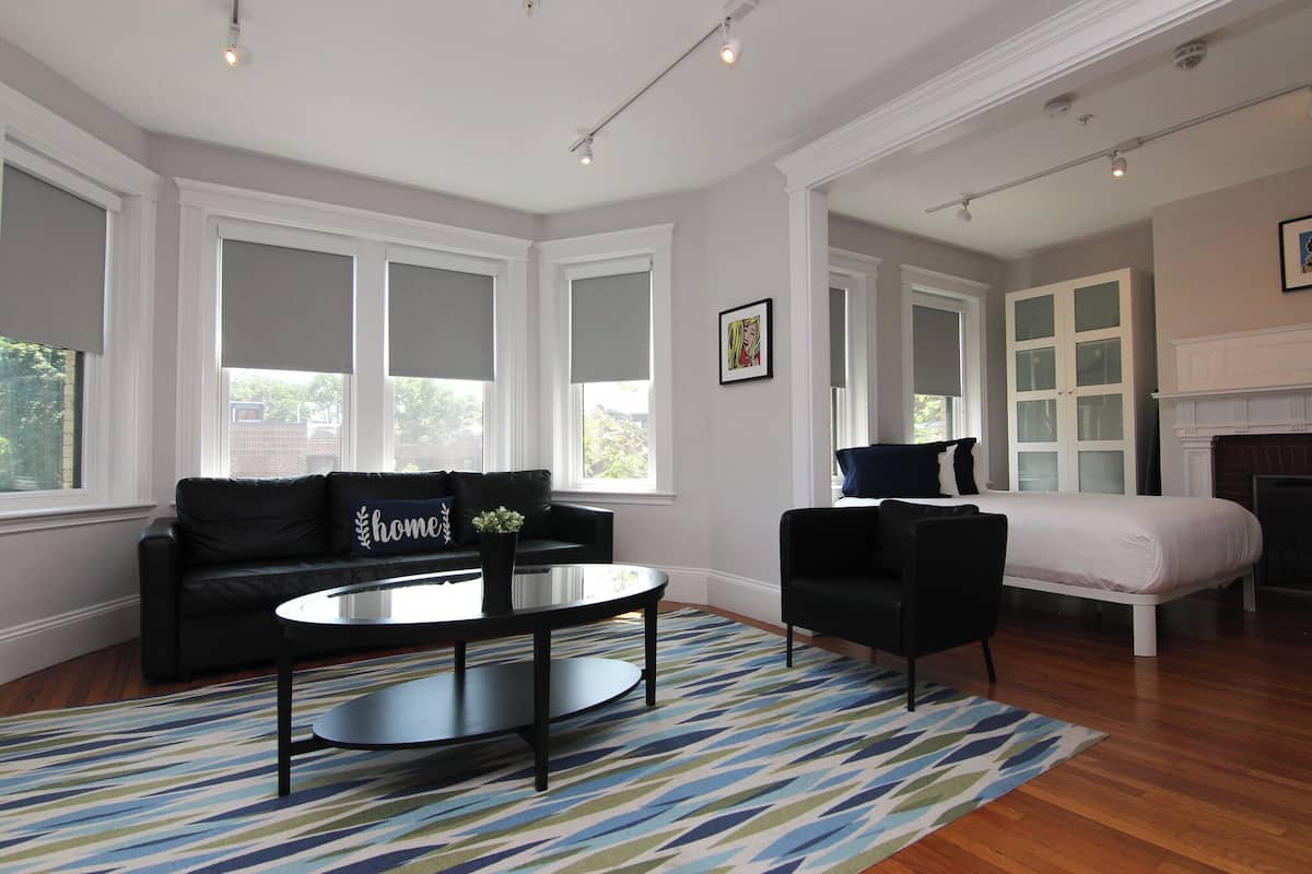 A spacious living room with a black leather sofa, a round coffee table, and a patterned rug.