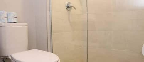 A bathroom with a toilet, a shower with a glass door, and a tiled floor.