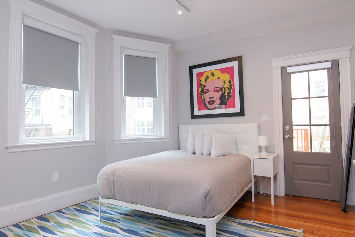 A bedroom with a bed, a nightstand, a door, and a window.