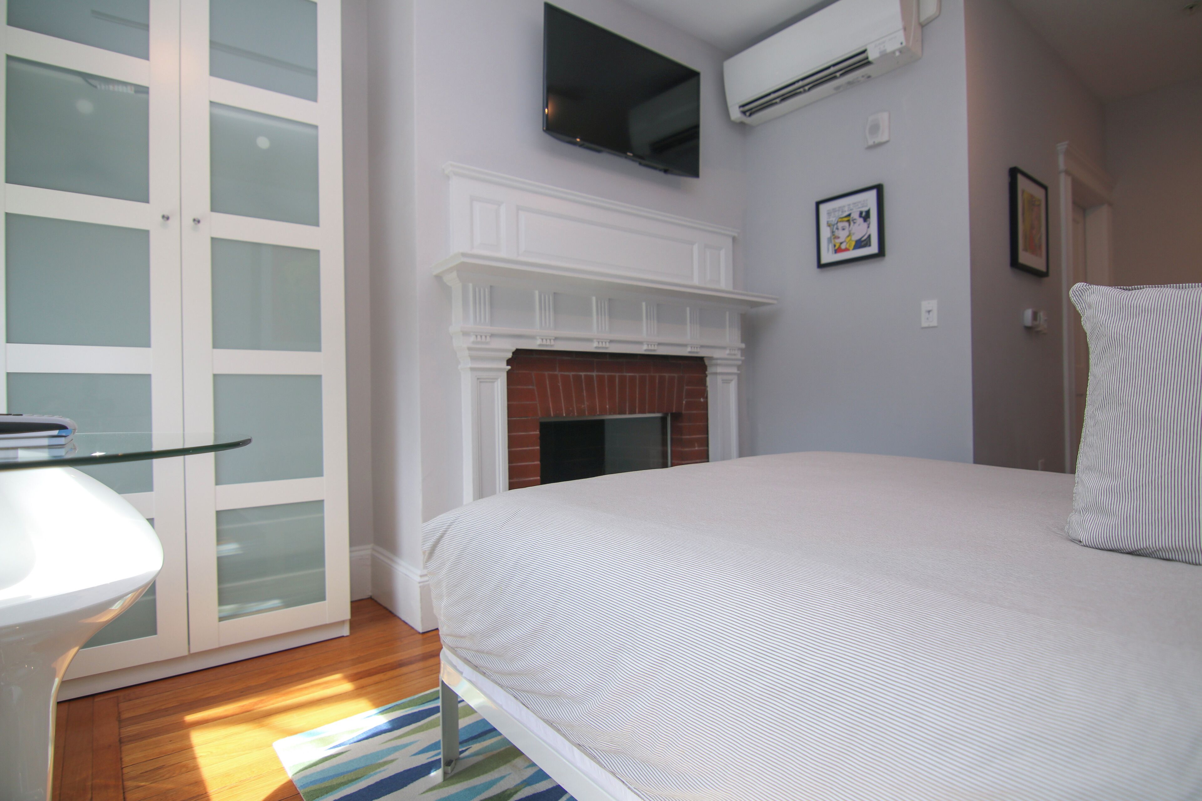 A bedroom with a bed, a fireplace, a TV mounted on the wall, and a door with frosted glass panels.