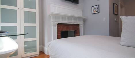 A bedroom with a bed, a fireplace, a TV mounted on the wall, and a door with frosted glass panels.