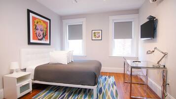 Un dormitorio moderno con cama, mesita de noche, lámpara y un escritorio con silla.