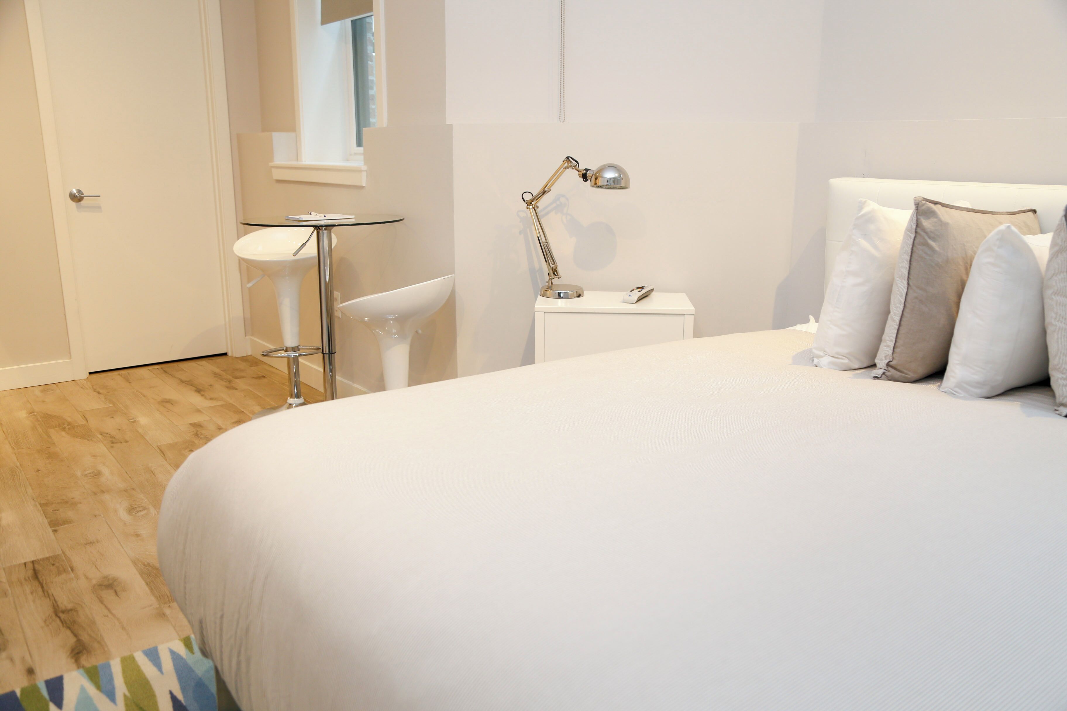 Ein modernes Schlafzimmer mit einem großen Bett, einem Nachttisch mit Lampe, einem kleinen weißen Nachttisch und einem weißen Stuhl.