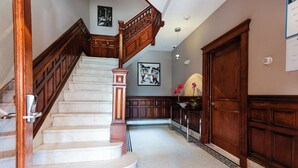 A grand staircase with a wooden handrail and marble steps, leading to a landing with a decorative floor pattern.