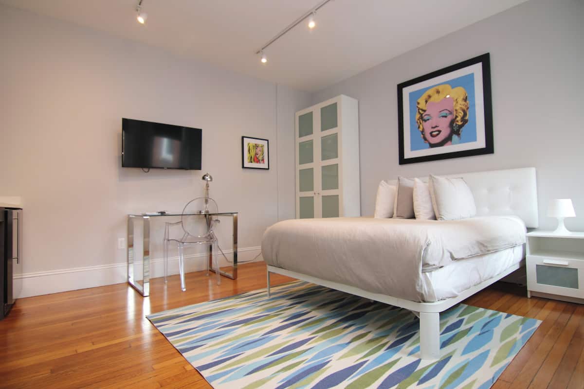 A modern bedroom with a bed, a TV, a desk, and a chair.