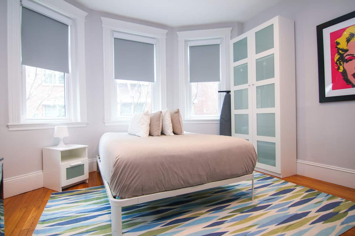 A bedroom with a bed, a nightstand, a dresser, and a window with blinds.