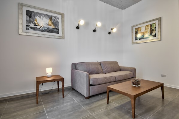 A modern living room with a grey sofa, two wooden tables, and three wall-mounted lights.