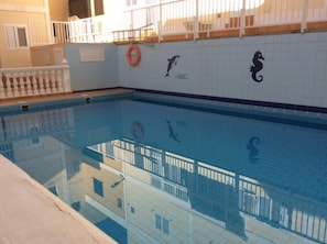 Une piscine aux murs recouverts de carreaux, une bouée de sauvetage et une fresque représentant des dauphins et des hippocampes.