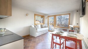 A compact kitchen with a dining area, a white sofa, and a view of a snowy landscape through large windows. - InstaView - One Bedroom Apartment, Sleeps 4 (Pontagna)