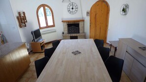 A room with a long wooden table, black chairs, a fireplace, a wooden door, and a clock on the wall. - Nice villa with pool in Las Tres Calas near the beach! (Les Tres Cales)