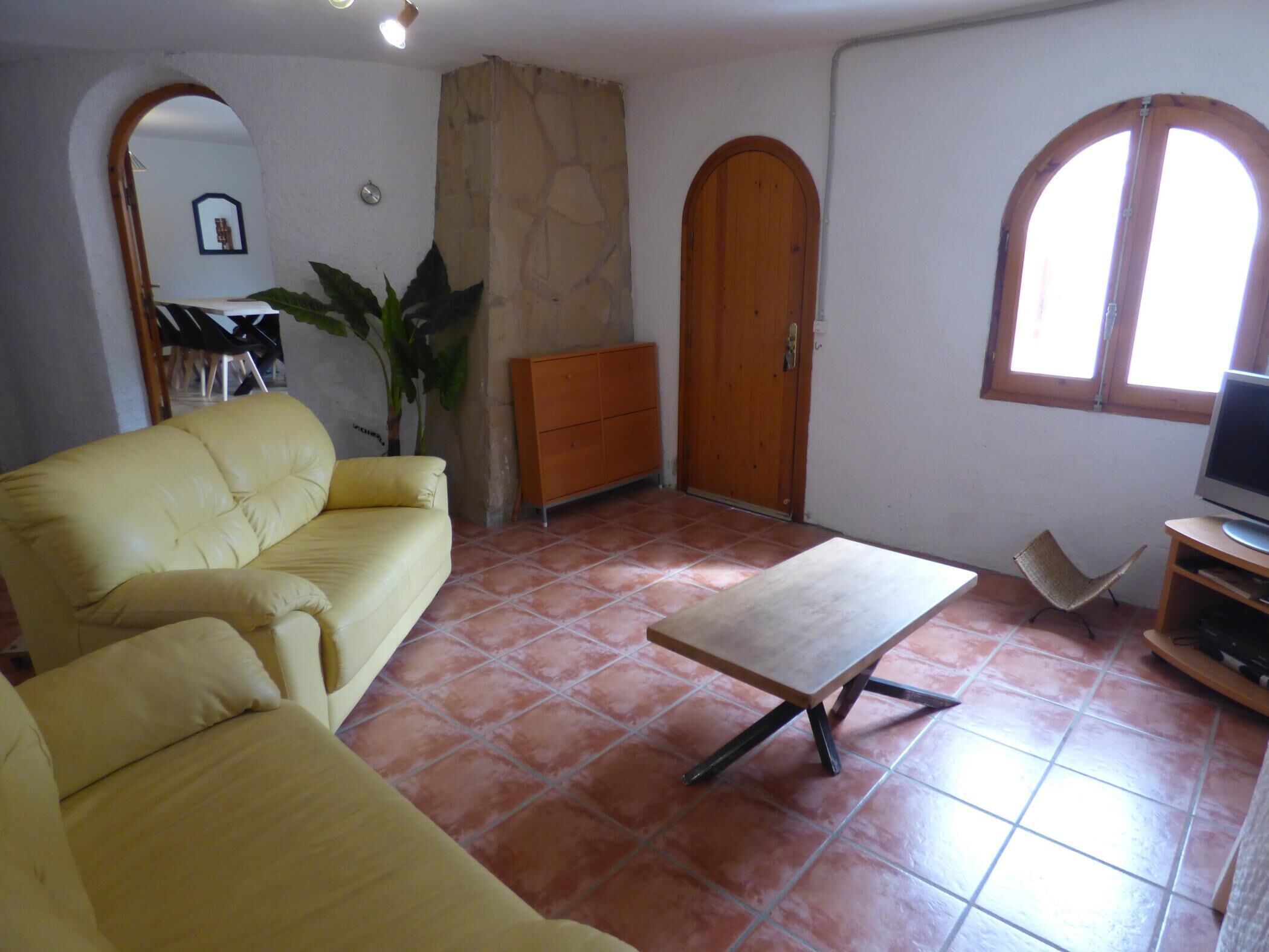 Un salon avec un canapé jaune, une table basse en bois, un meuble pour la télévision et un mur en pierre.