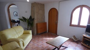 A living room with a yellow sofa, a wooden coffee table, a TV stand, and a stone wall. - Nice villa with pool in Las Tres Calas near the beach! (Les Tres Cales)