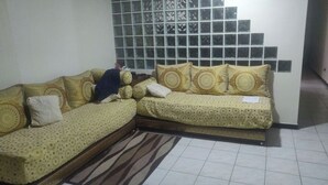 Een woonkamer met een zithoek, een kamerkleed met patroon en een betegelde vloer.