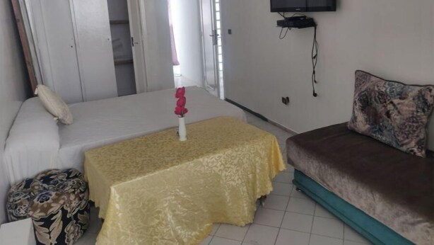 Een slaapkamer met een bed, een bank, een aan de muur bevestigde televisie en een tafel met een gele tafelkleed.