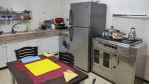 Een kleine keuken met een koelkast, wasmachine, fornuis en een eettafel met placematen.