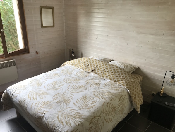 Une chambre à coucher avec un lit, une table de chevet, une lampe et une fenêtre.