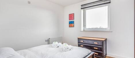Un dormitorio con cama, cómoda, radiador y ventana con persianas.