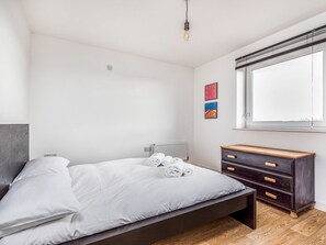 A modern bedroom with a bed, a dresser, a radiator, and a window with blinds.