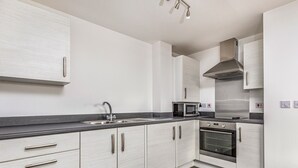 Una cucina moderna con mobili bianchi, un piano di lavoro nero, un lavello in acciaio inossidabile, un forno a microonde e un forno.