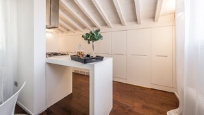 A modern kitchen with white cabinetry, a central island with a vase and jar, and a wooden ceiling. - Emilia Suite Urban (Modena)