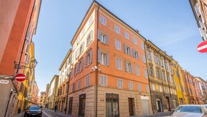 A narrow street with buildings on either side, including a prominent orange building with a sign that reads "HOPS." - Emilia Suite Urban (Modena)
