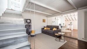 A modern living room with a staircase, a grey sofa, and a small round table. - Emilia Suite Urban (Modena)