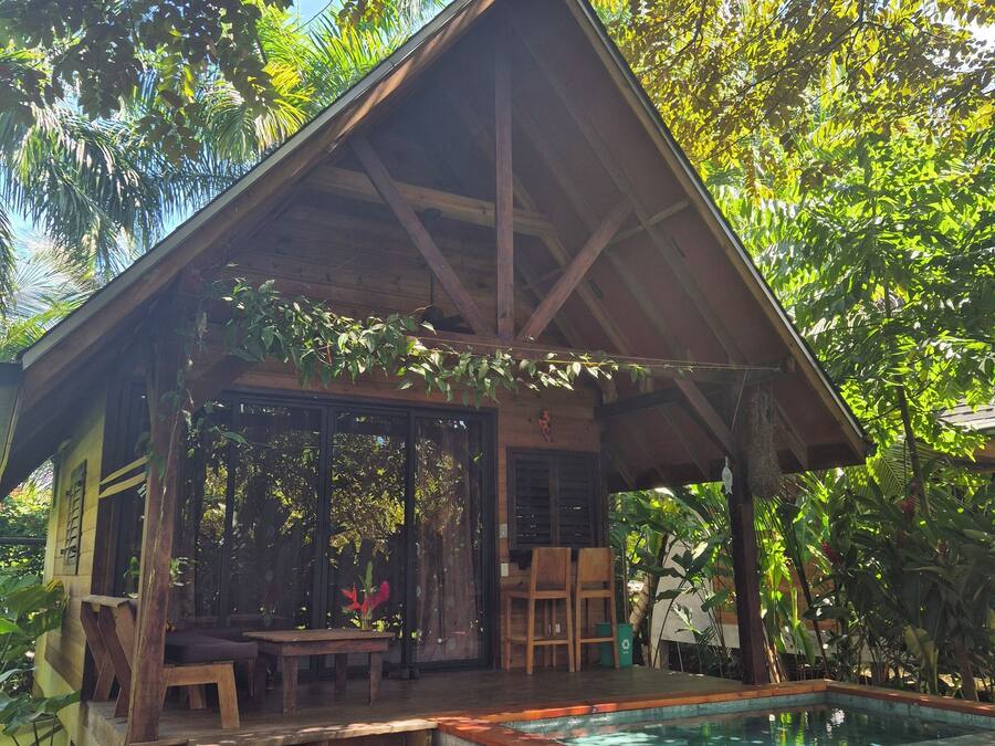 Una estructura de madera con techo inclinado, una piscina y una escalera que lleva a un área de estar cubierta.