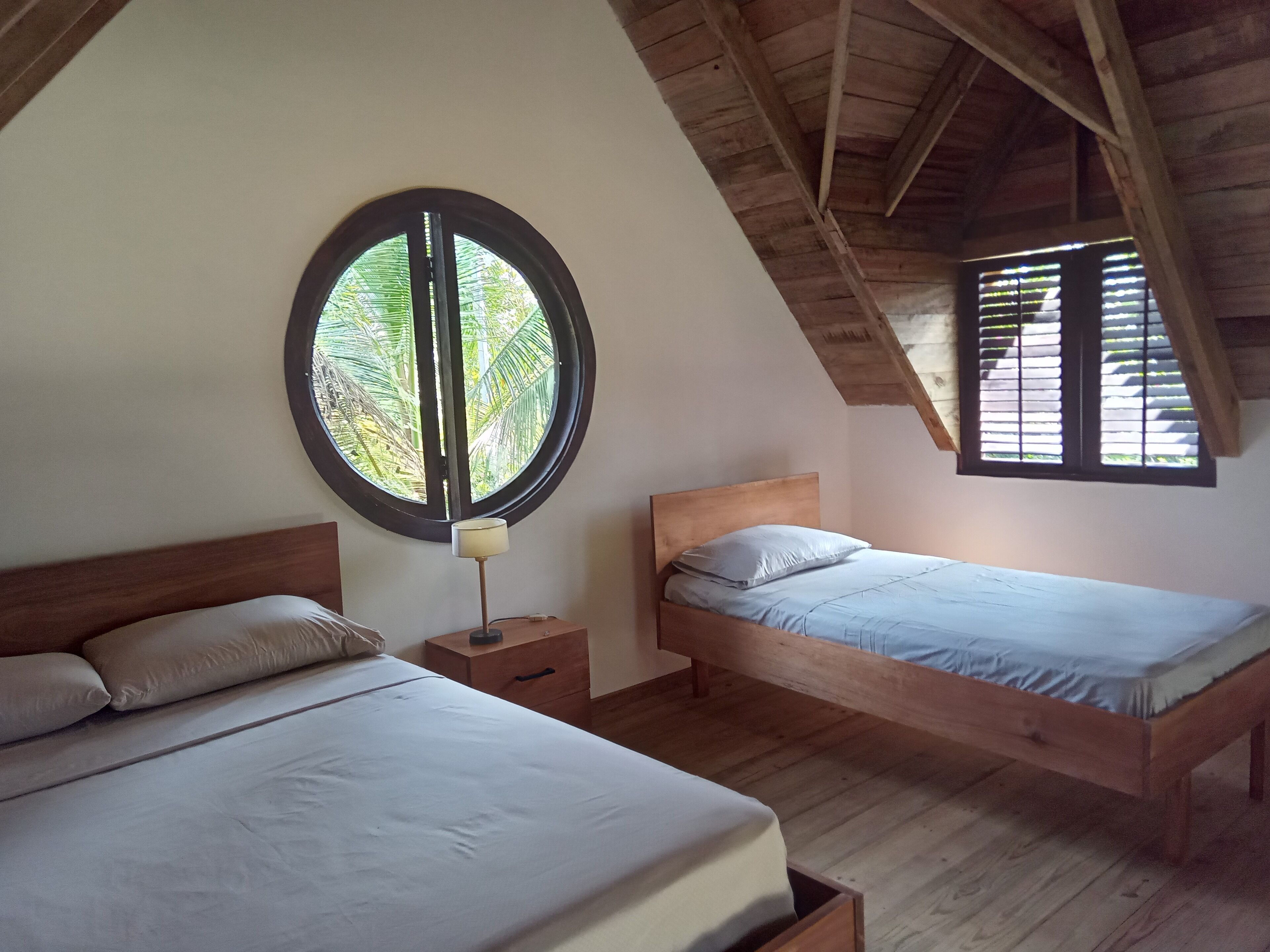 A bedroom with two beds, a round window, and a sloped ceiling.