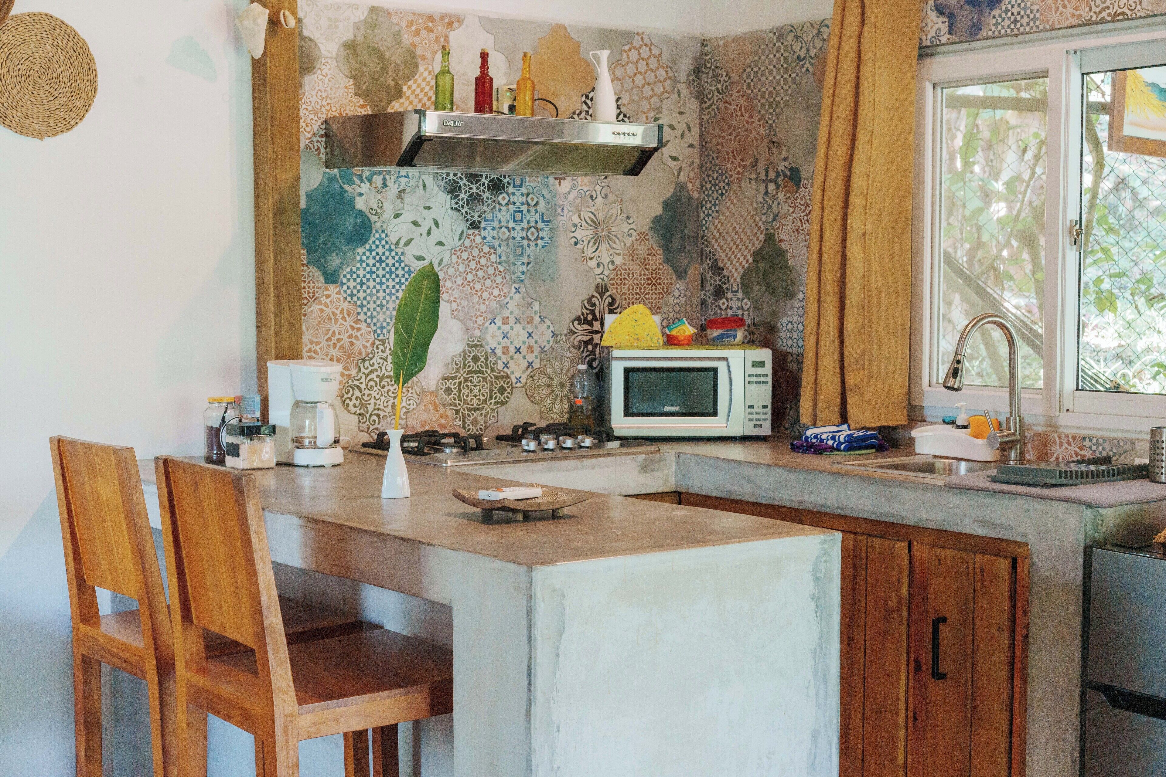 A kitchen with a microwave, stove, and wooden chairs.