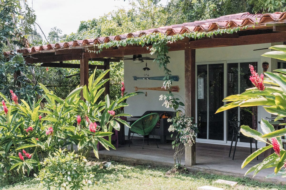 A covered outdoor seating area with a wooden pergola, a green chair, and a dining table.
