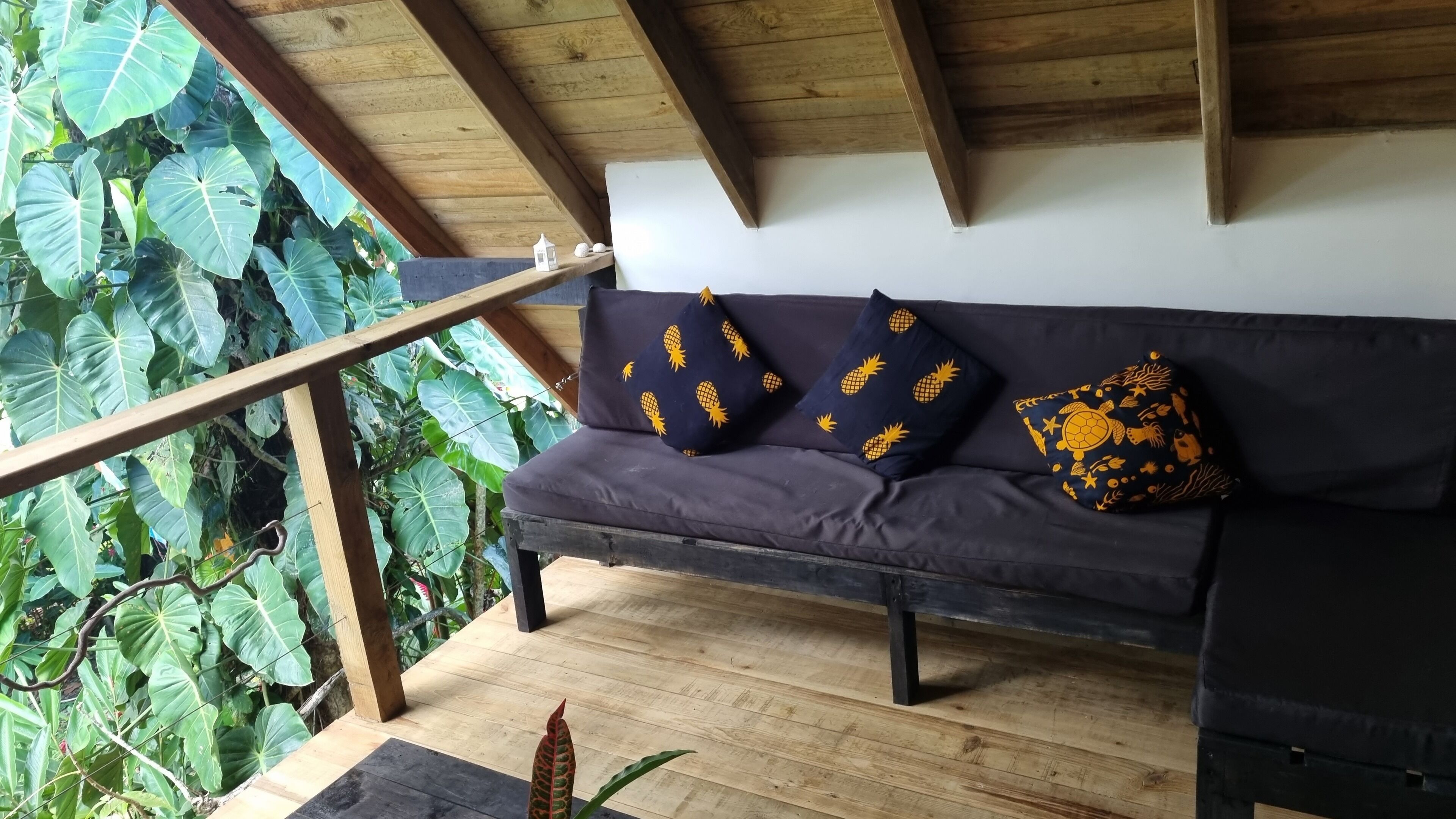 Una terraza de madera con una zona de estar acolchada que incluye dos cojines con motivos de piña y tortuga.