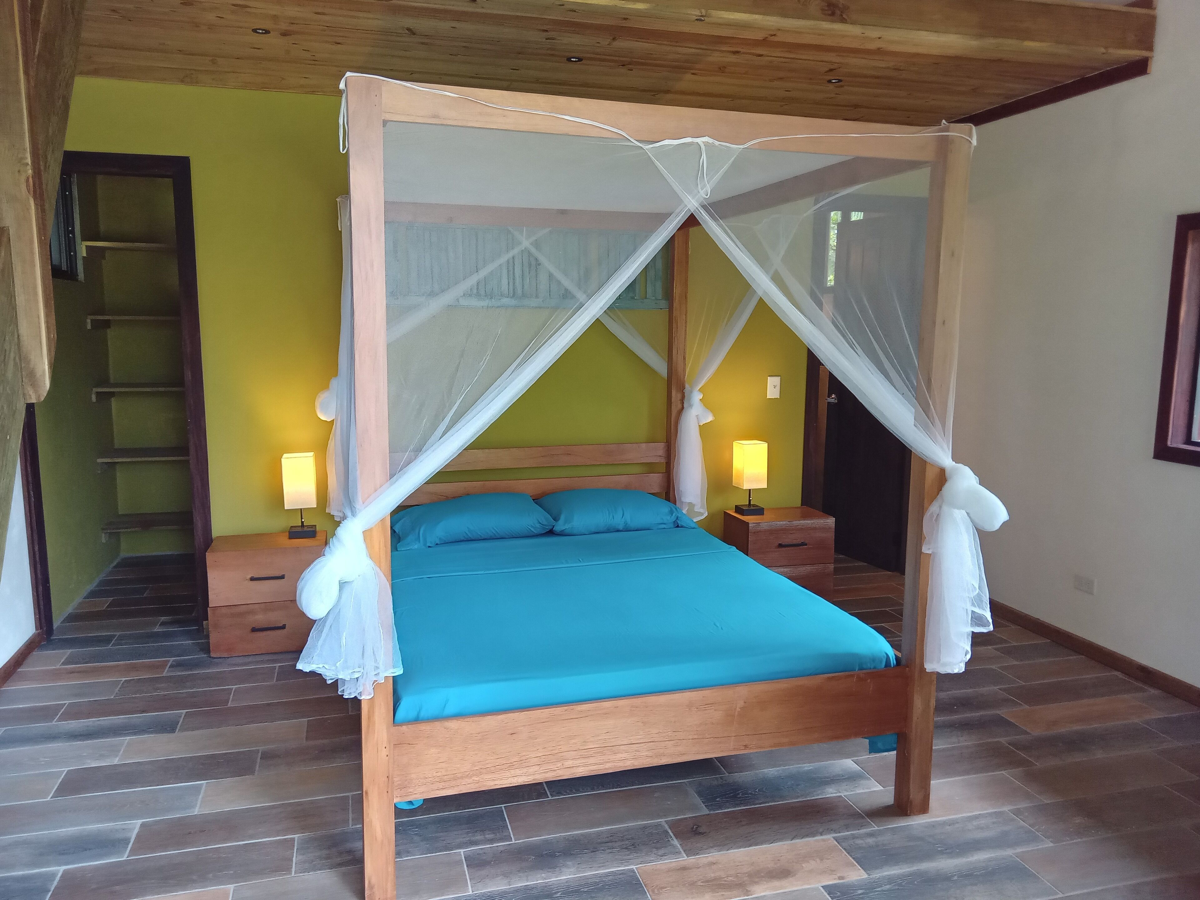 Un letto a baldacchino con tenda, un comodino con una lampada e una scala di legno appoggiata al muro.