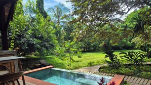 A wooden deck with a pool, surrounded by lush greenery and a clear view of a grassy area. - Cabañas Naturaleza (Bocas del Toro)