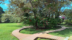 A landscaped garden with a curved brick pathway, green grass, and various plants including red flowers. - Cabañas Naturaleza (Bocas del Toro)