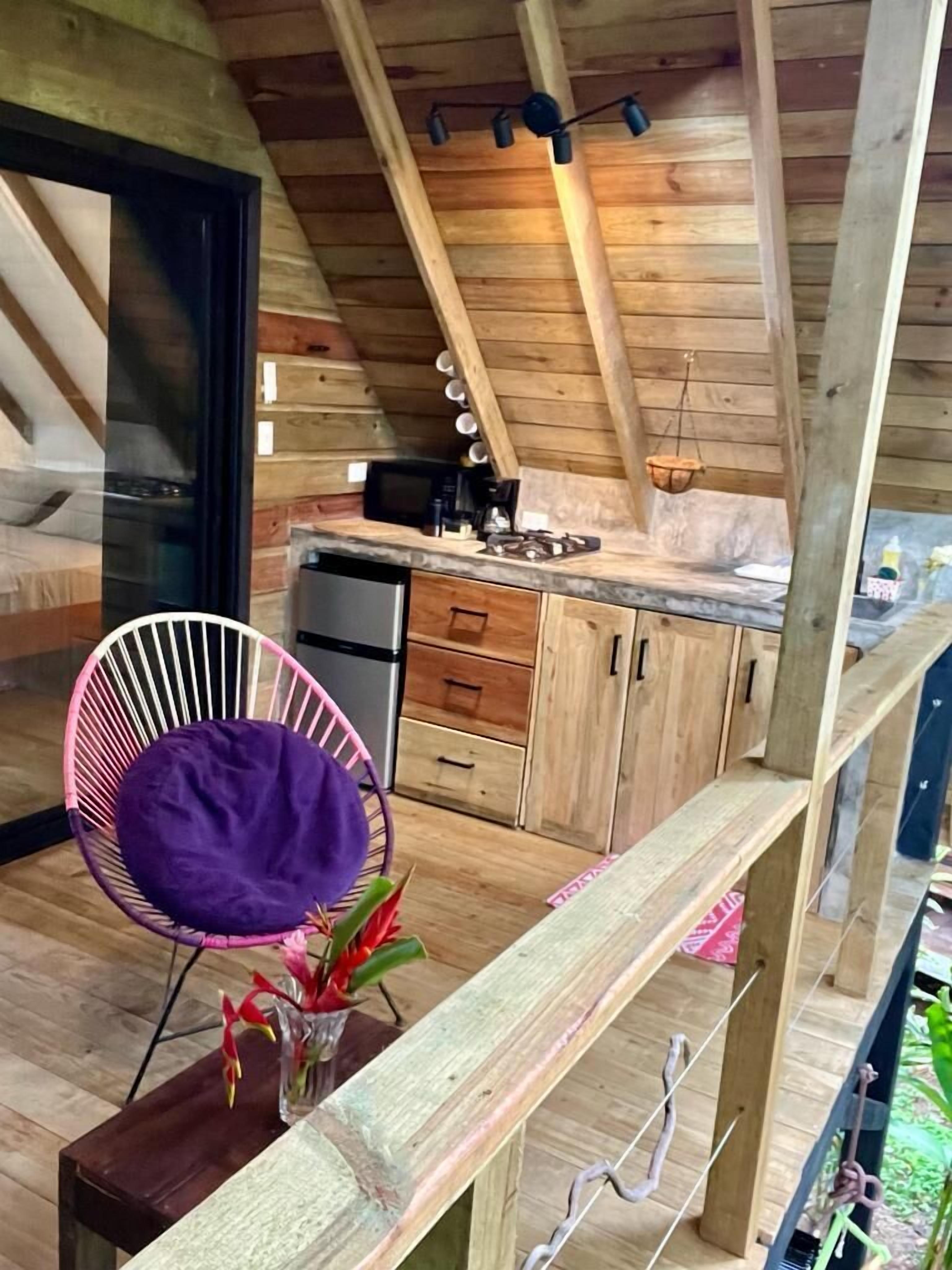 Ein rustikales Holzhaus-Interieur mit Küchenbereich, einem Esstischstuhl und einem kleinen Tisch mit Blumen.