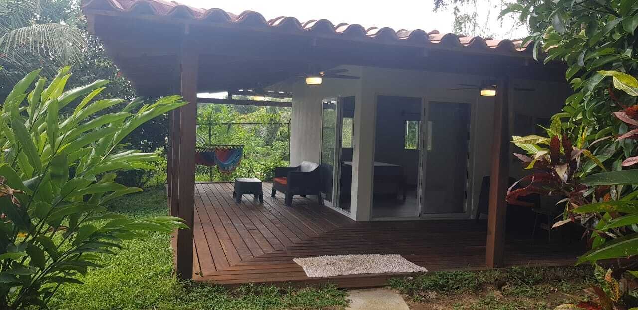 A covered outdoor area with a wooden deck, a seating arrangement, and a glass door leading to an interior space.