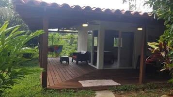 A covered outdoor area with a wooden deck, a seating arrangement, and a glass door leading to an interior space.